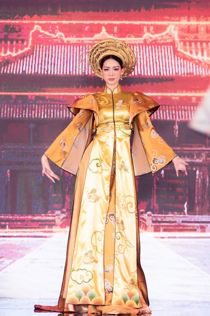 Hoa hậu Bảo Ngọc xuất hiện với vẻ uy nghiêm trong chiếc áo dài thuộc bộ sưu tập Dấu ấn vàng son của Trần Thiện Khánh, thể hiện màu sắc văn hóa Trung Bộ.