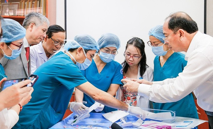 Giám đốc Sở Y tế TP HCM Tăng Chí Thượng (ngoài cùng, bên phải) xem bác sĩ trình diễn lại động tác thông tim nong van, sau ca can thiệp thành công. Ảnh: Bệnh viện Từ Dũ