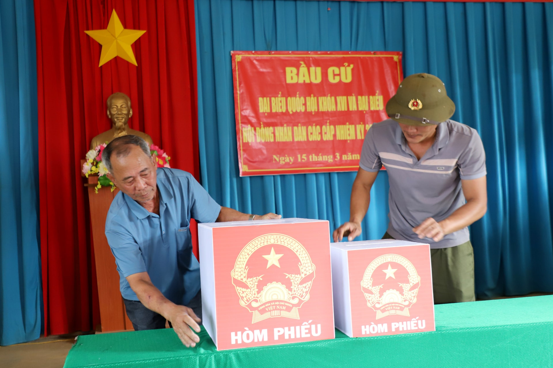 Ông Trần Quang Trung (bên trái) chuẩn bị cơ sở vật chất tại điểm bỏ phiếu thôn Quảng Hợp, phục vụ công tác bầu cử