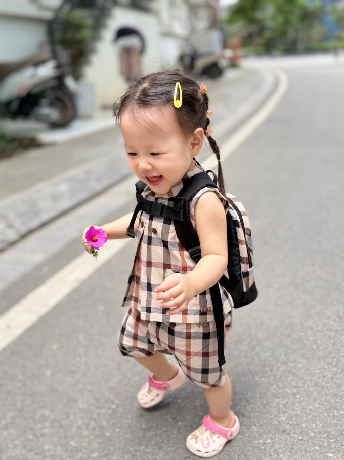 Em bé hai tuổi được mẹ cho diện trang phục họa tiết kẻ màu trung tính, đồng điệu với cặp sách và tết tóc hai bên khi đến trường.