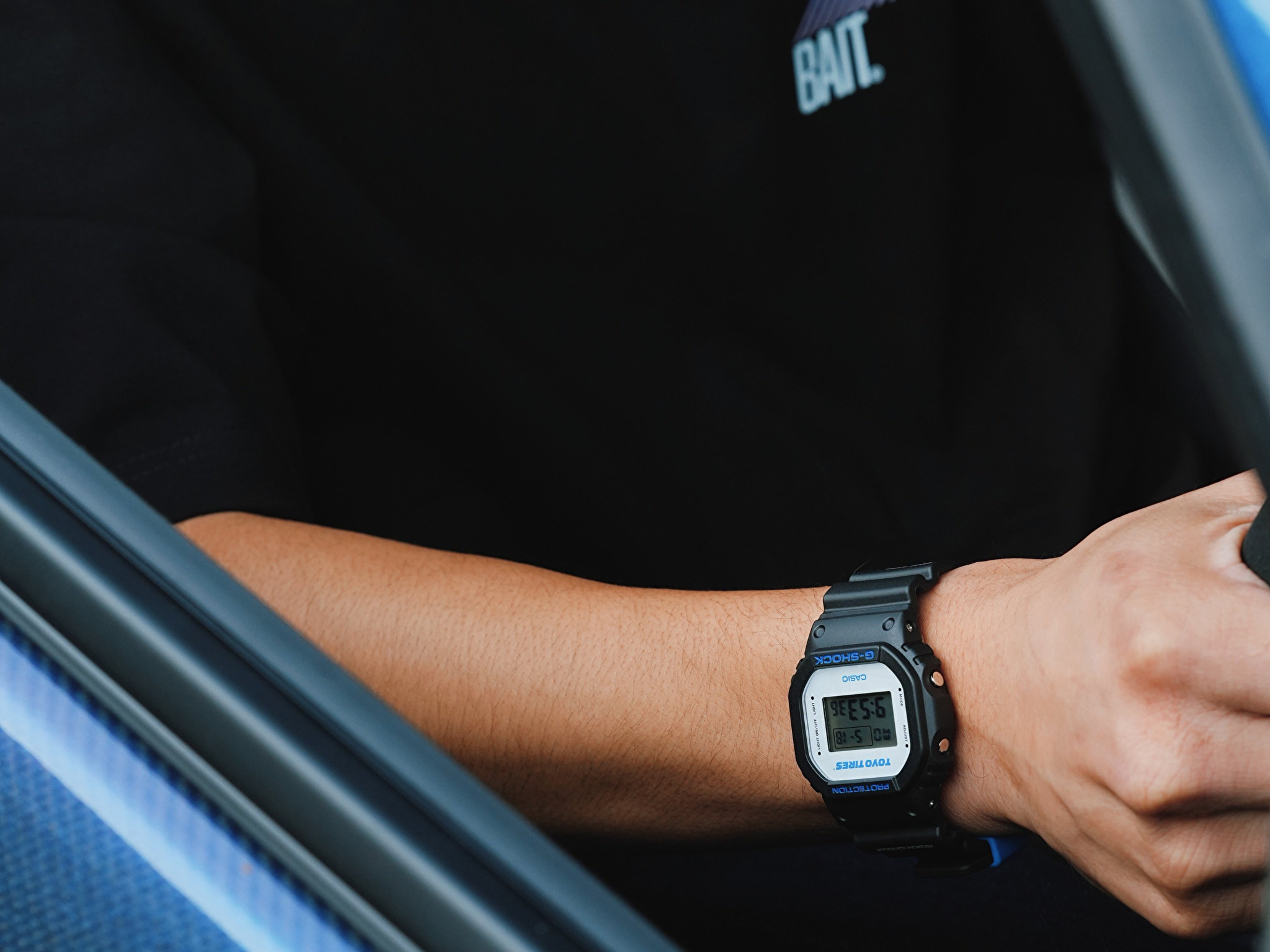 Người đeo đồng hồ Casio G-Shock DW5600TT25-1 x Toyo Tires ngồi trong xe ô tô.