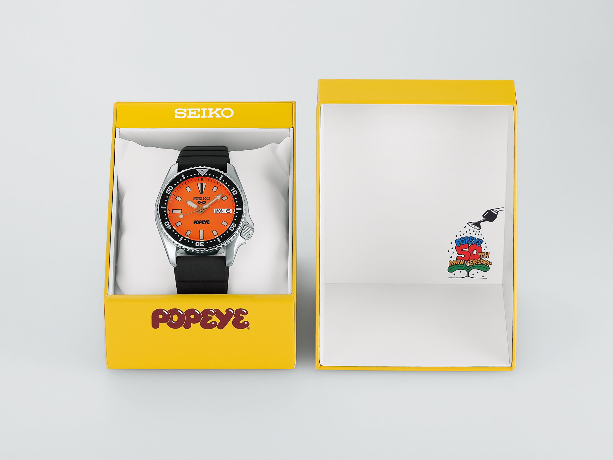 Đồng hồ Seiko 5 Sports x Popeye HDB013 đặt cạnh hộp đựng màu vàng phiên bản giới hạn.
