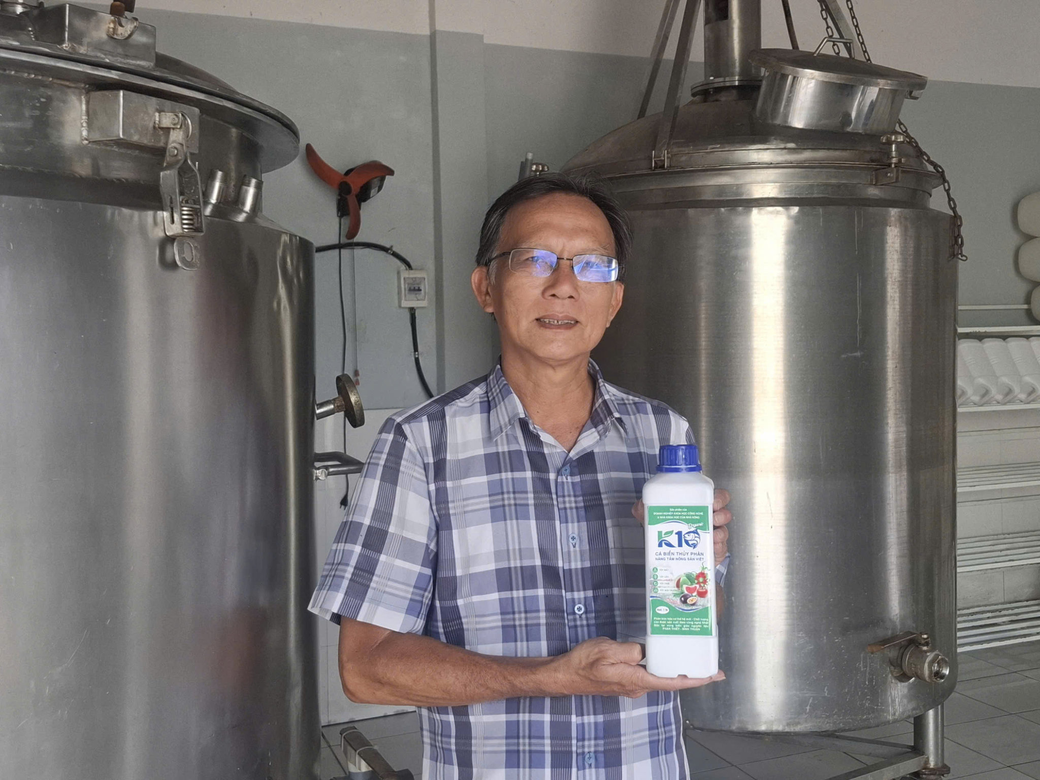 Thạc sĩ Hồ Trinh bên hệ thống thiết bị thủy phân và sản phẩm phân bón hữu cơ sinh học từ phế phẩm cá biển tại nhà xưởng sản xuất