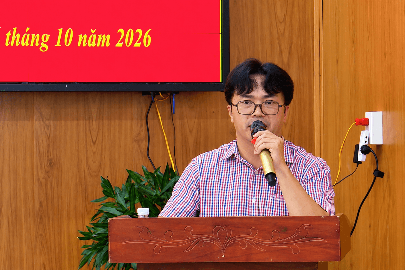 Diễn giả bên bục gỗ trước màn hình đỏ